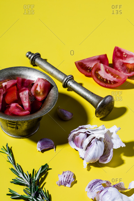Mediterranean salad dressing (spanish olive oil, tomatoes, rosemary, garlic) and bronze mortar on yellow background.