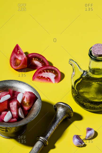 Mediterranean salad dressing (spanish olive oil, tomatoes, garlic) and bronze mortar on yellow background.