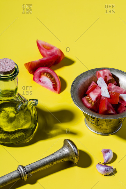 Mediterranean salad dressing (spanish olive oil, tomatoes, garlic) and bronze mortar on yellow background.
