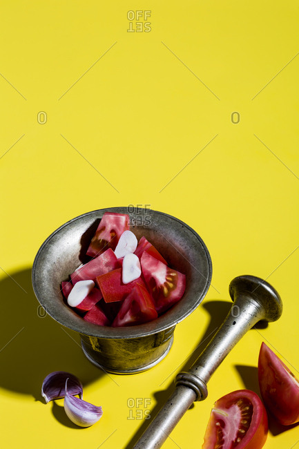 Mediterranean salad dressing (tomatoes, garlic) and bronze mortar on yellow background.