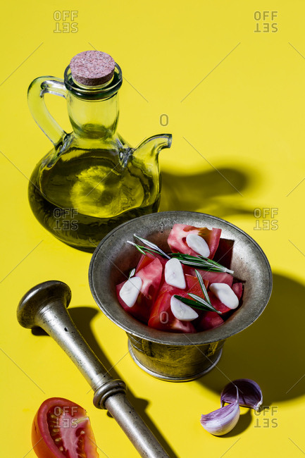 Mediterranean salad dressing (spanish olive oil, tomatoes, rosemary, garlic) and bronze mortar on yellow background.