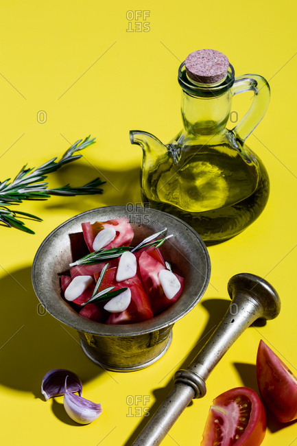Mediterranean salad dressing (spanish olive oil, tomatoes, rosemary, garlic) and bronze mortar on yellow background.