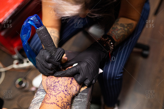 unrecognizable woman tattoo artist tattooing on the skin of one hand