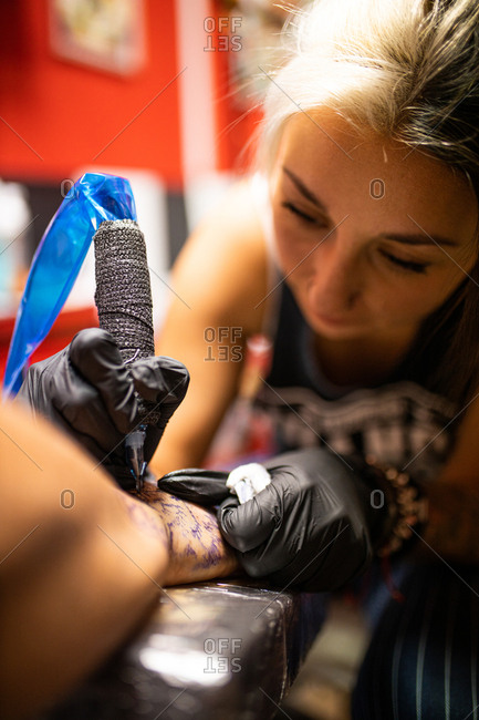 young woman tattoo artist tattooing on the skin of one hand