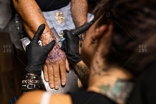 unrecognizable woman tattoo artist tattooing on the skin of one hand