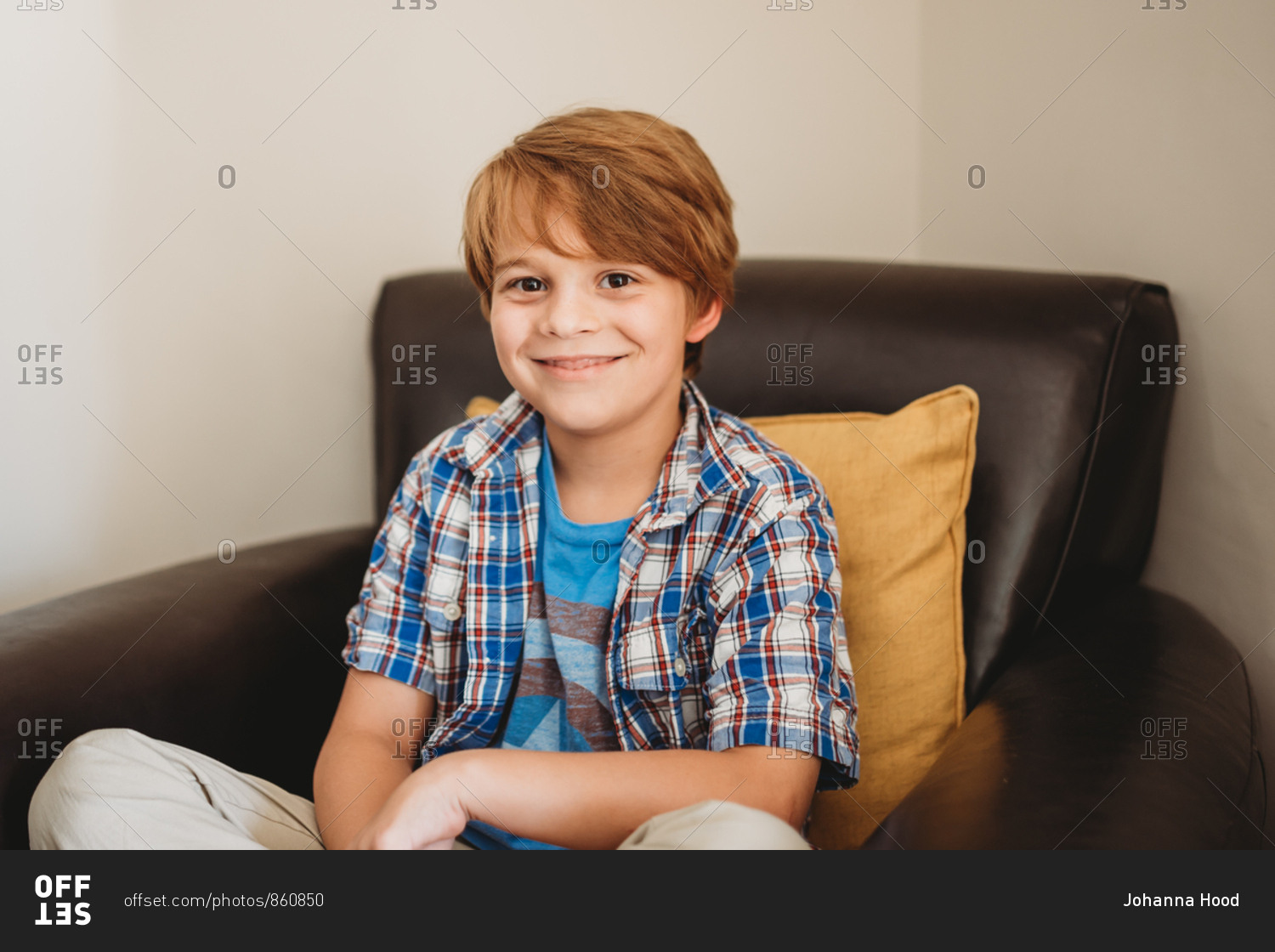 Portrait of a little boy with red hair and brown eyes sitting on brown  leather chair stock photo - OFFSET