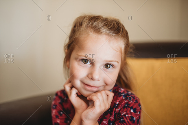Portrait of a little girl with blonde hair and brown eyes sitting on brown  leather chair stock photo - OFFSET