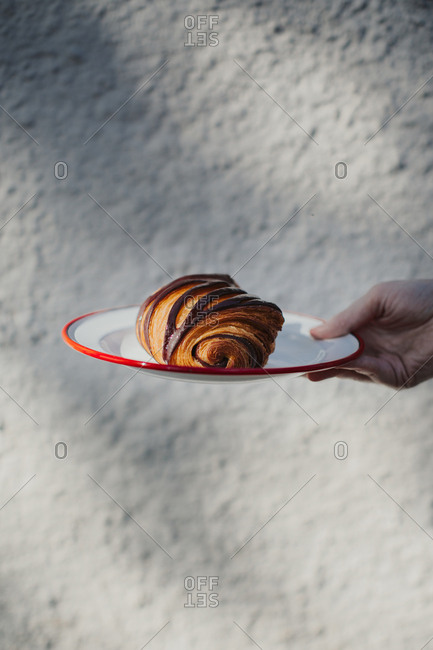 Hand holding a plate with a flaky pain au chocolat against a white textured background