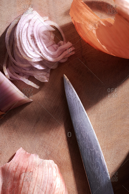 Paring knife on a cutting board near a thinly sliced shallot