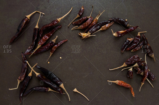 Loose scattered dried chilli peppers on rustic dark brown worn tray