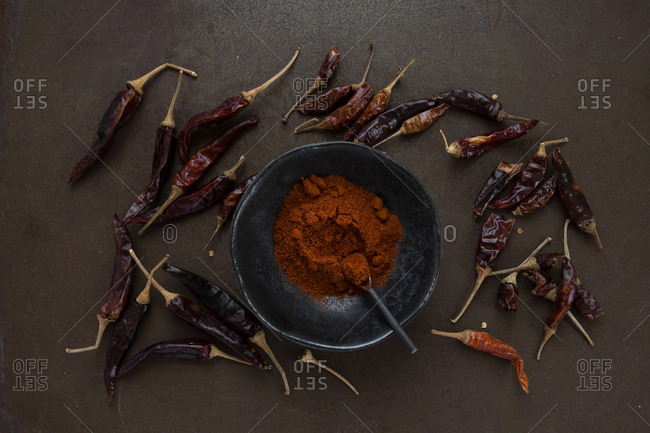 Cayenne powder in wabi sabi ceramic bowl surrounded by scattered dried chilli peppers