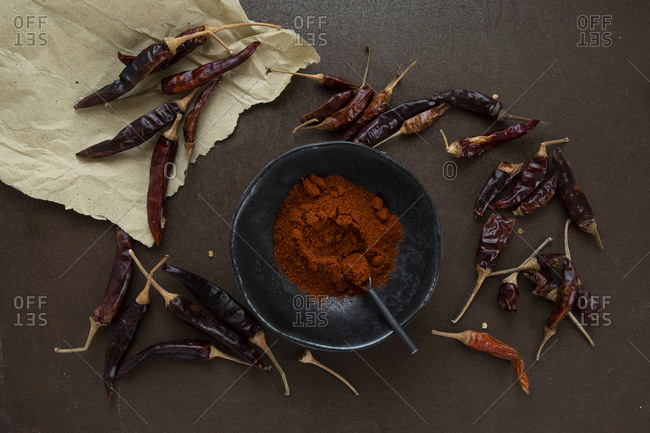 Cayenne powder in wabi sabi ceramic bowl surrounded by scattered dried peppers