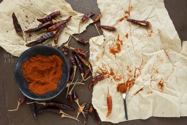 Cayenne and paprika powder in rustic old bowl circled by dried peppers on parchment paper