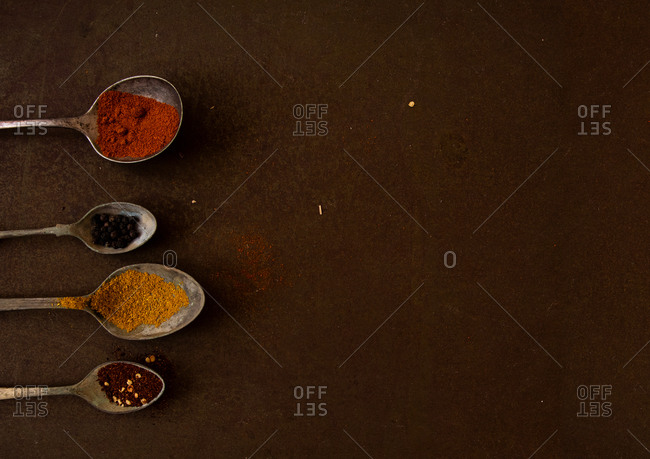 Antique spoons filled with spices on dark brown rustic kitchen tray