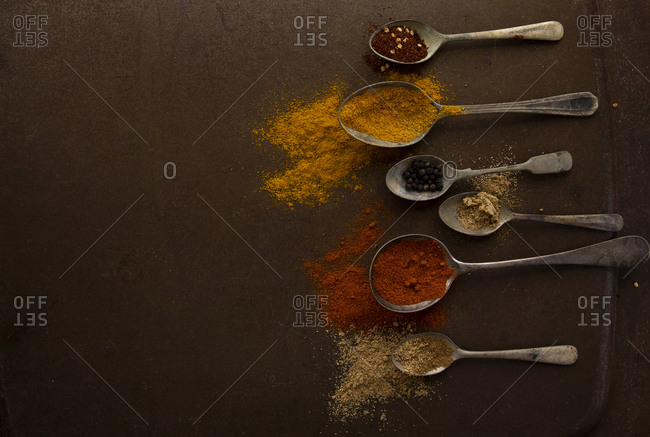 old antique spoons filled with spices on dark brown rustic kitchen tray