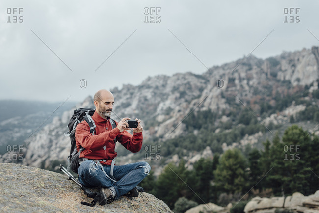 Mid aged bald hiker taking picture with smartphone to rocky scenery
