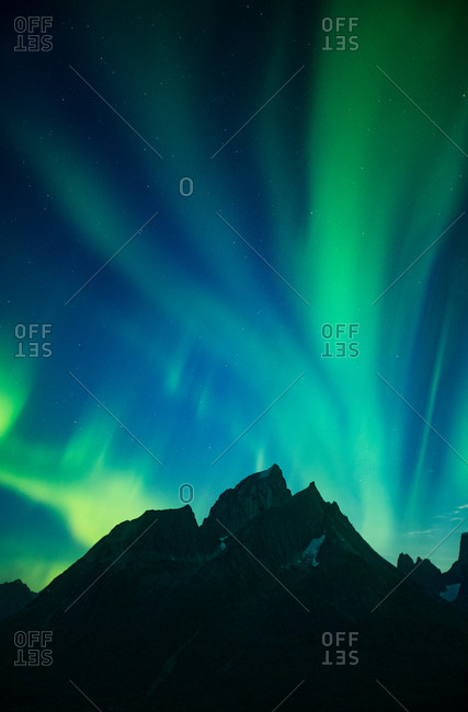Aurora Boralis dancing in night sky above mountain peaks and lake, Greenland