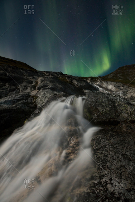 Aurora Borealis over waterfall scene, Greenland