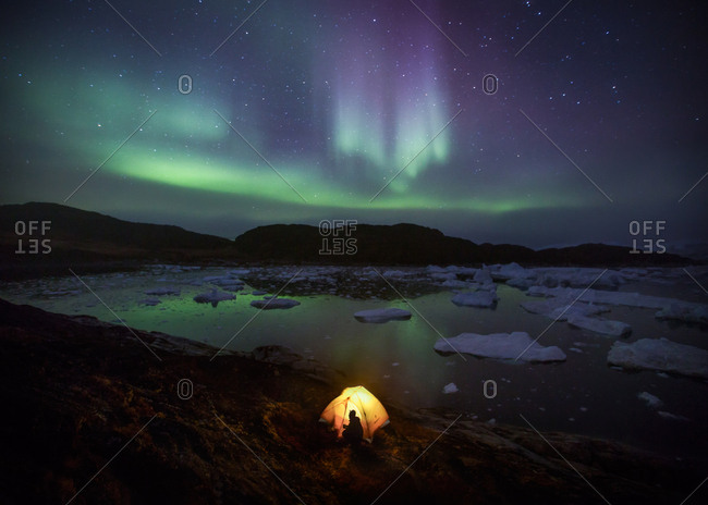 Tent overlooking icefjord and icebergs under starry night sky and aurora borealis