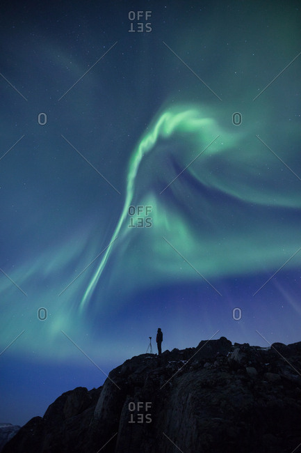 Person with a camera on rocky cliff under the Aurora Borealis