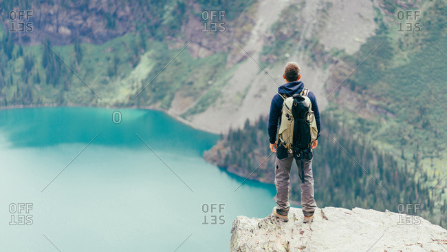 Male hiker is standing on a cliff looking at the lake in Glacier NP
