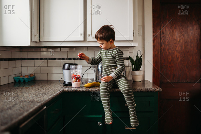 Young boy making strawberry and banana smoothie in kitchen