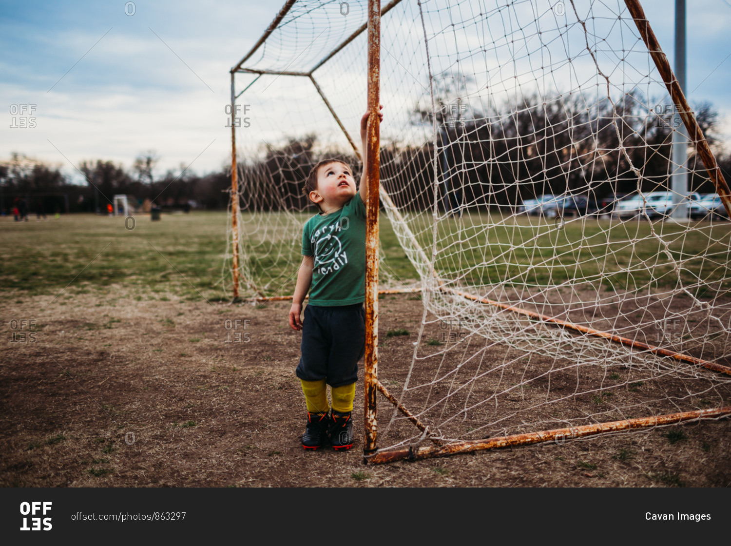 Young boy standing inside soccer goal wearing cleats