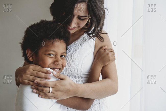 Mid-level view of smiling son being hugged by smiling mother in studio