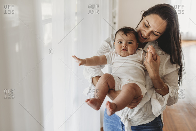 Young mother holding baby daughter and smiling in natural light studio