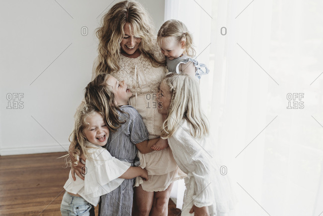 Mother embracing four daughters and laughing in natural light studio