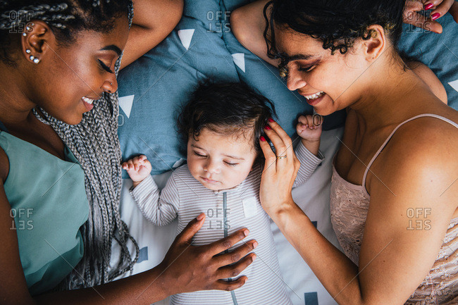 Overhead view of happy girlfriends with cute sleeping baby boy resting on bed