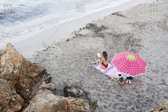 Young woman sitting on towel at the beach reading book
