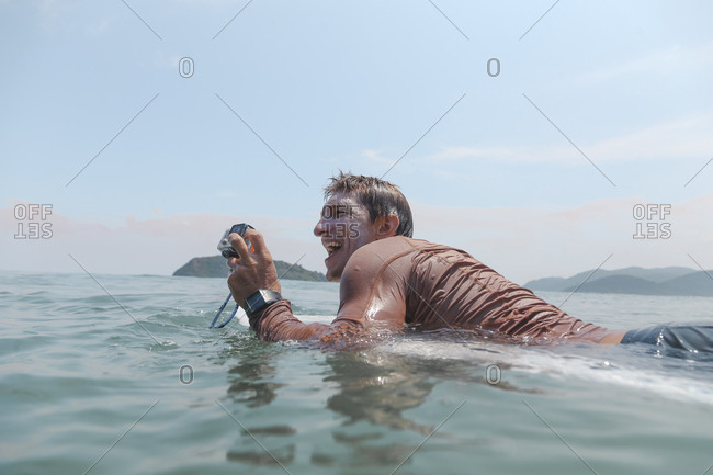 Surfer with action camera lying on surfboard