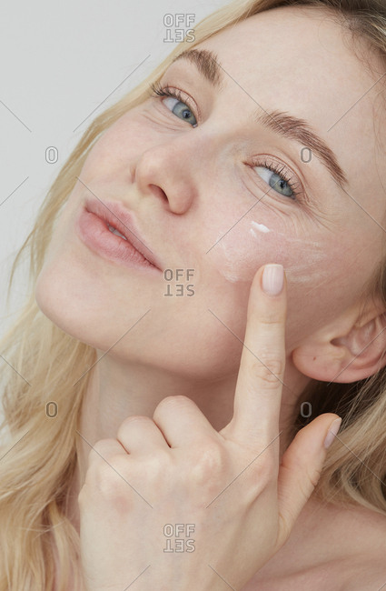 Portrait of young woman applying cream on her face