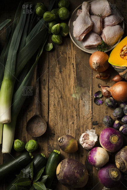 Raw winter vegetables and chicken being prepared for soup. They are displayed on a rustic timber background with a vintage rustic spoon.