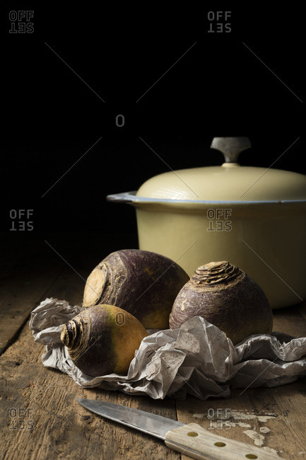 Swedes in crumpled paper wrapping on a rustic timber surface. A cast iron casserole is in the background.