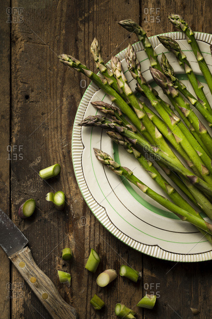 Fresh, raw asparagus on a vintage plate, on a timber background. A knife and cut asparagus ends are alongside.