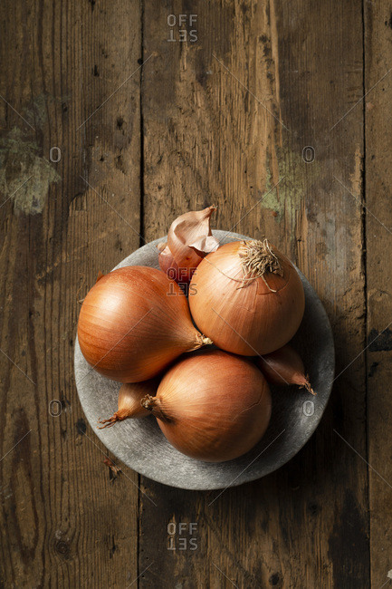 Brown onions and shallots in a stone bowl, on a rustic timber background.