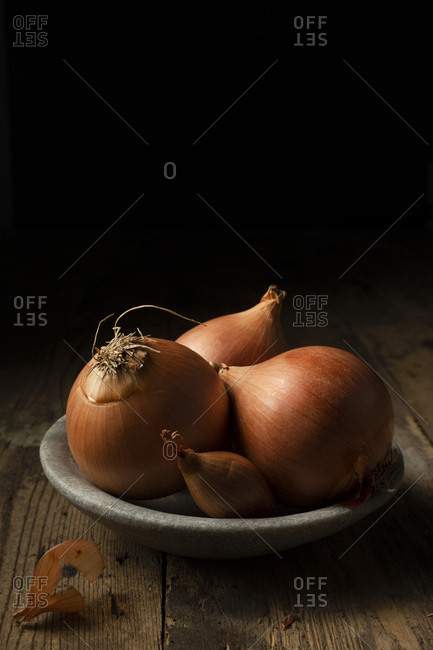 Brown onions and shallots in a stone bowl, on a rustic timber background.