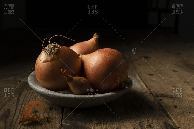 Brown onions and shallots in a stone bowl, on a rustic timber background.