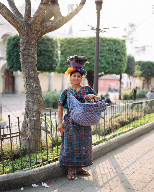 Antigua, Guatemala - January 17, 2019: Portrait of a young woman carrying textiles in a pouch and on her head