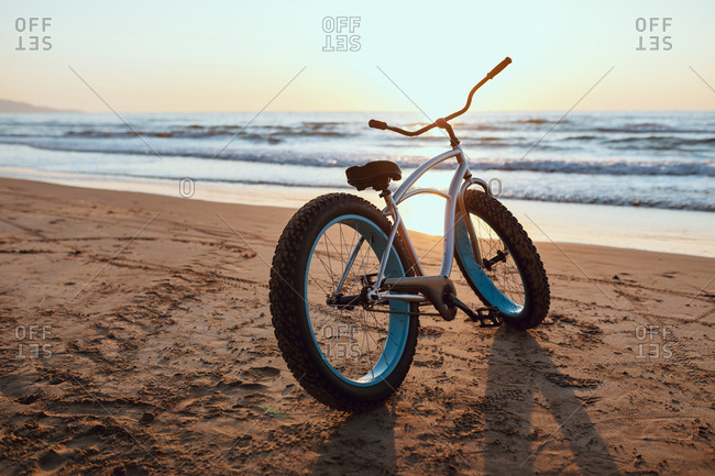Shiny new fat bike parked at sandy tranquil seaside on summer sunset