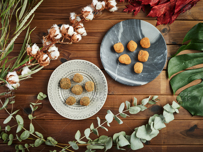From above branches and leaves of various plants arranged around plates with tasty croquettes on timber tabletop