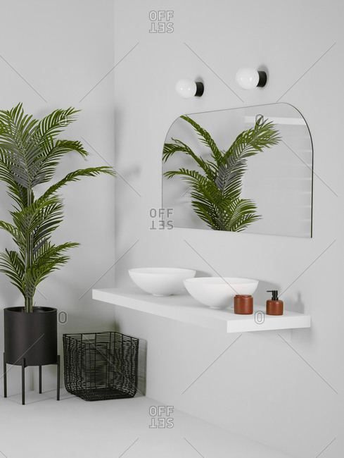 Ceramic bowls placed on simple shelf against white wall in bathroom with mirror and tall plant