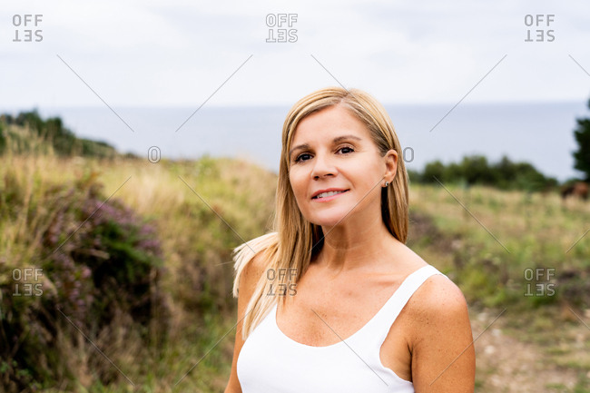 Inspired blonde woman with charming smile looking at camera while enjoying of views of countryside around