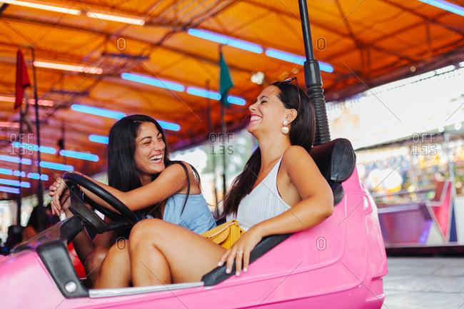 Cheerful women in casual outfit having fun and driving colorful attraction car at carnival
