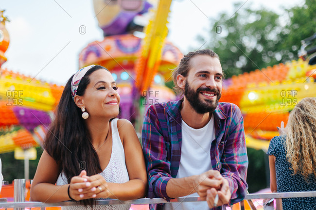 Amused casual couple looking up in excitement while visiting colorful attraction at sunny funfair