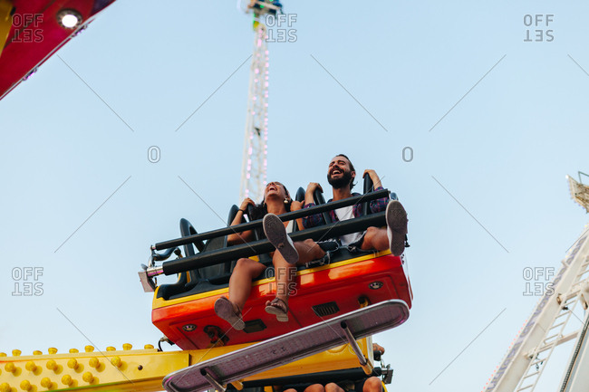 Enthusiastic carefree woman and man having fun while enjoying ride at colorful attraction at sunny funfair