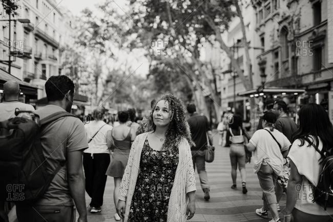 Black and white elegant adult female with curly hair looking away while walking in crowd on street of Barcelona, Spain