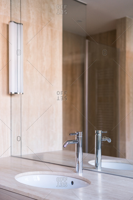 Oval washbasin and shiny steel faucet on wooden stand with mirror in modern bathroom